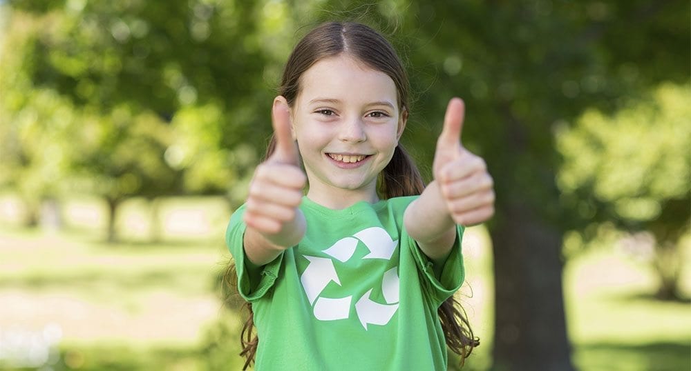 Happy little girl in green with thumbs up on a sunny day