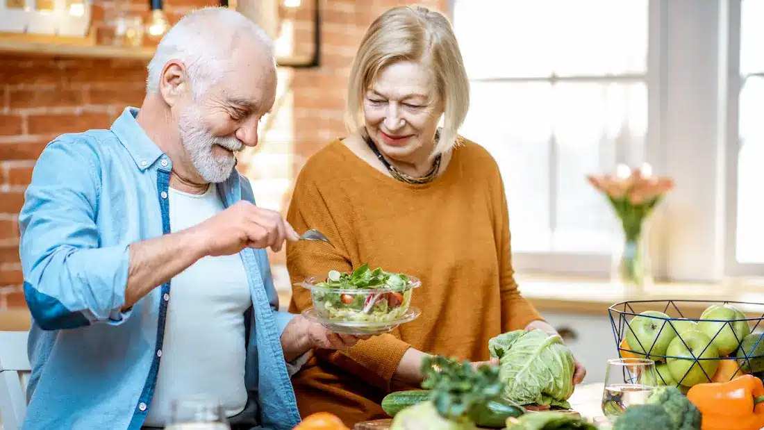 Smiling senior couple preparing and enjoying a fresh salad together in a bright kitchen, representing healthy eating habits that support iron intake and aging well